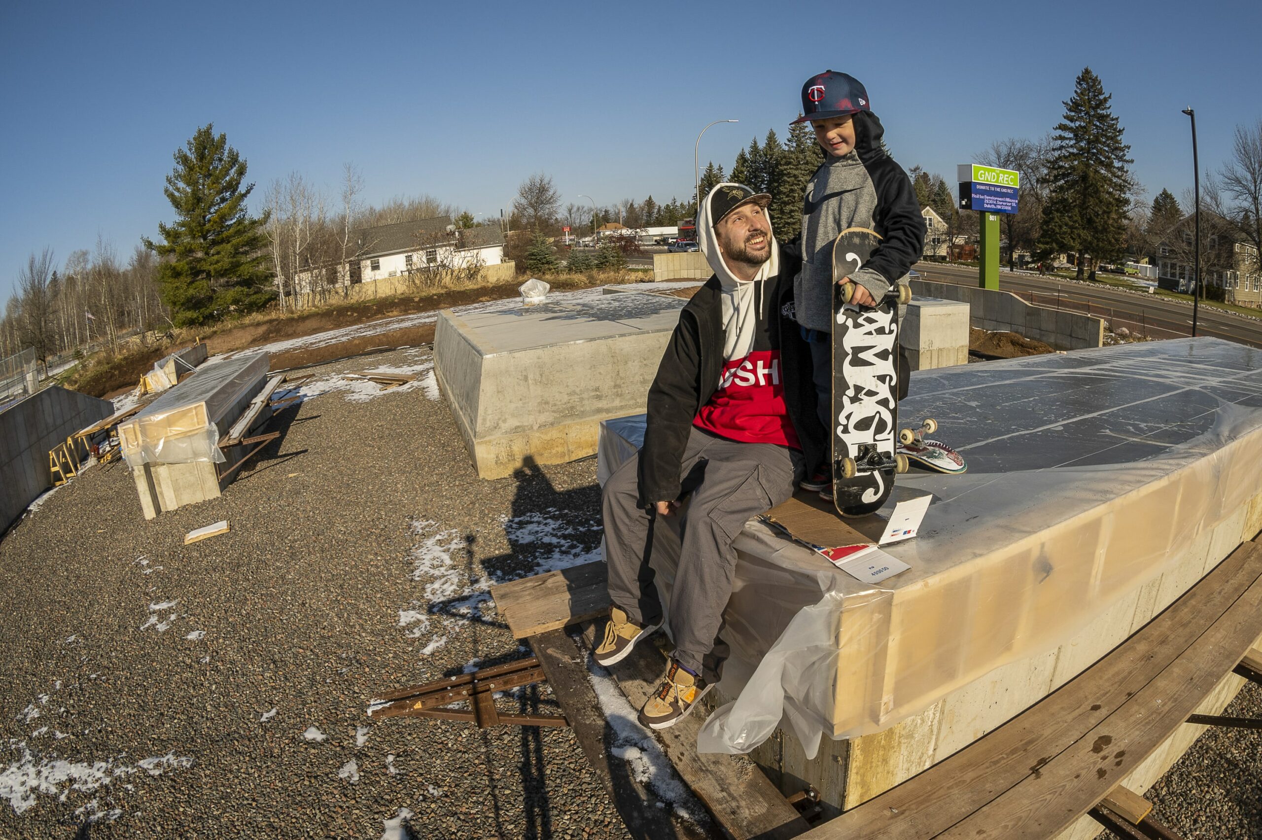 A man smiles at a young boy who is holding a skateboard on top of construction materials