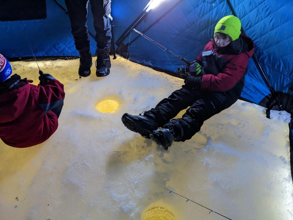 A boy sits on the ground while ice fishing in the winter