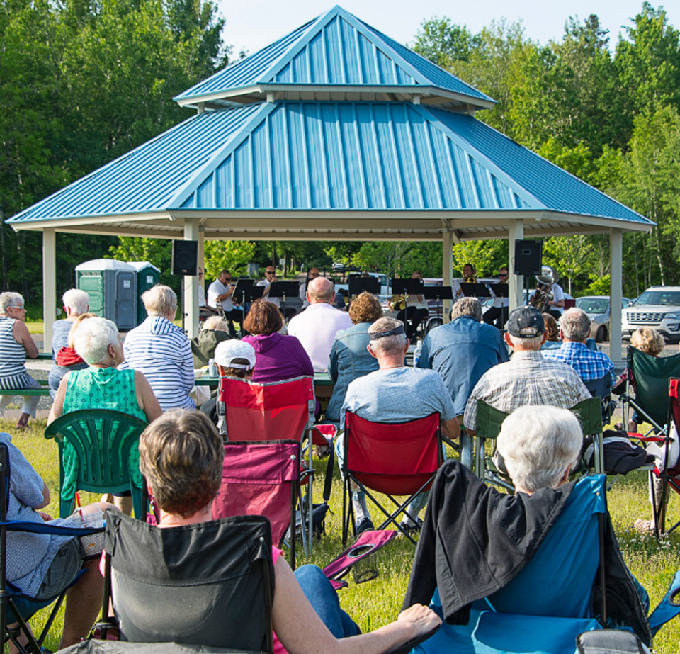 A group of people sitting down watch a group perform at the Pavilion at the GND REC