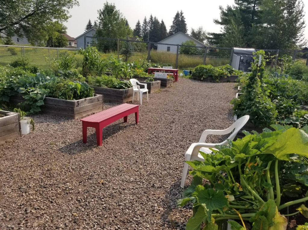 An image of a fully bloomed community garden at the GND REC, with a red bench in the middle