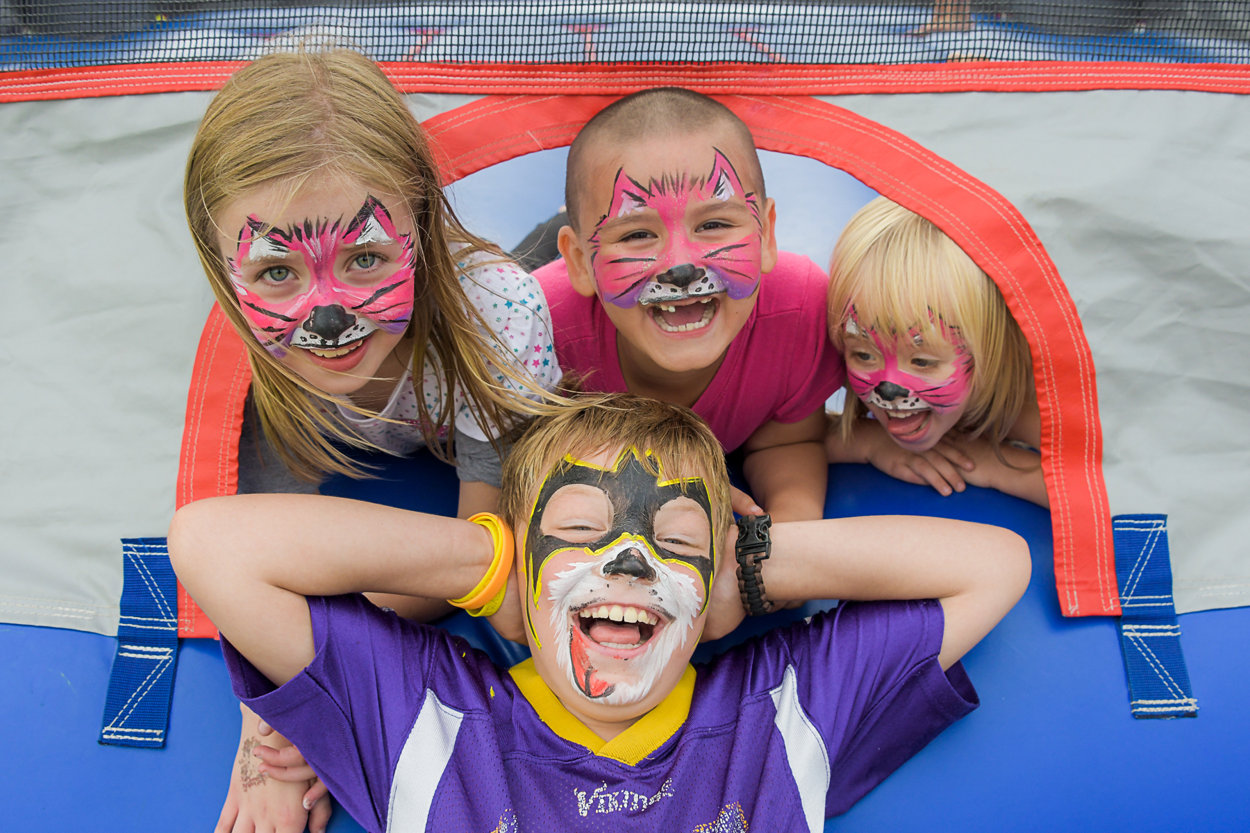 Four children smile while wearing face paint in a bouncy house