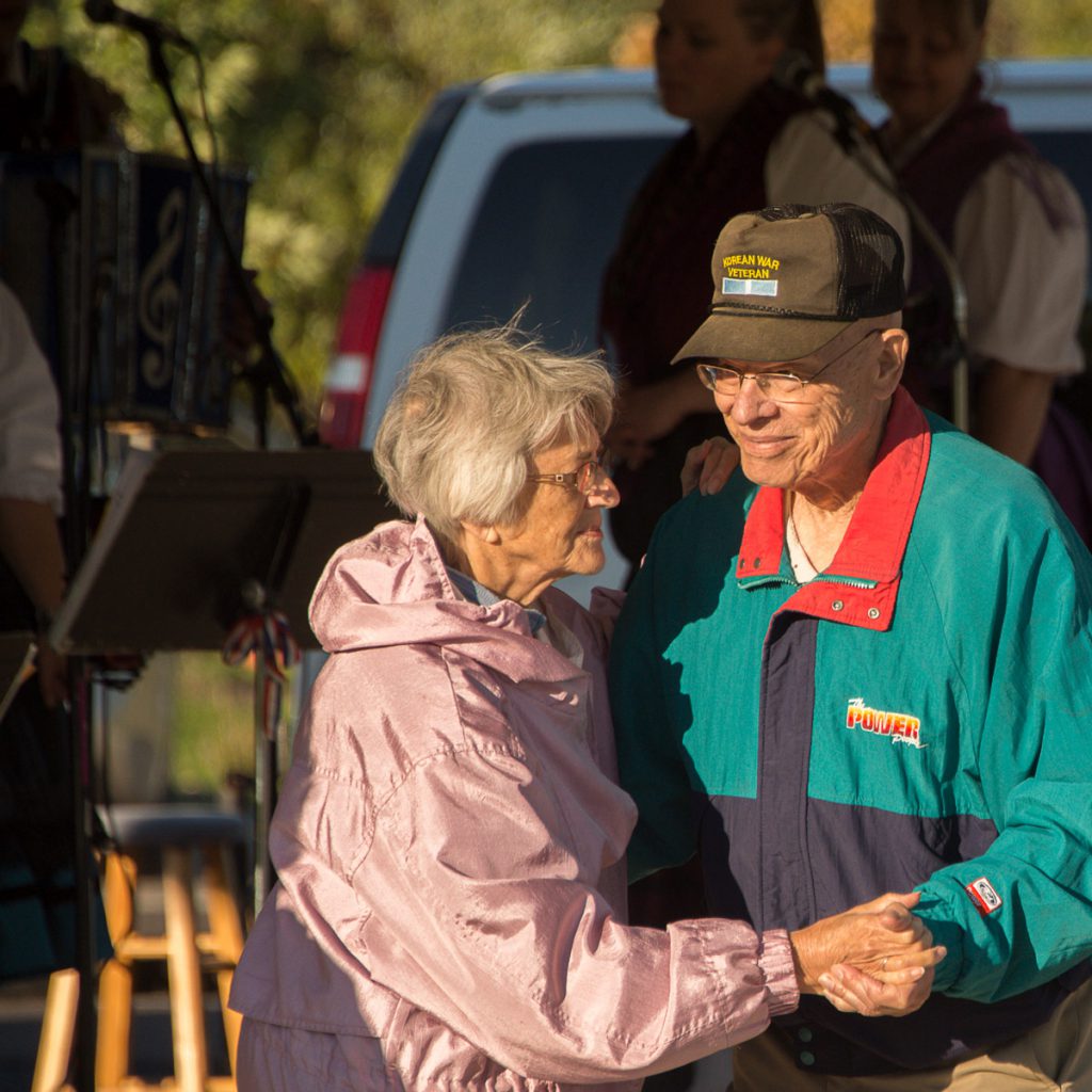 An older couple smile and dance at the Pavilion while people perform behind them