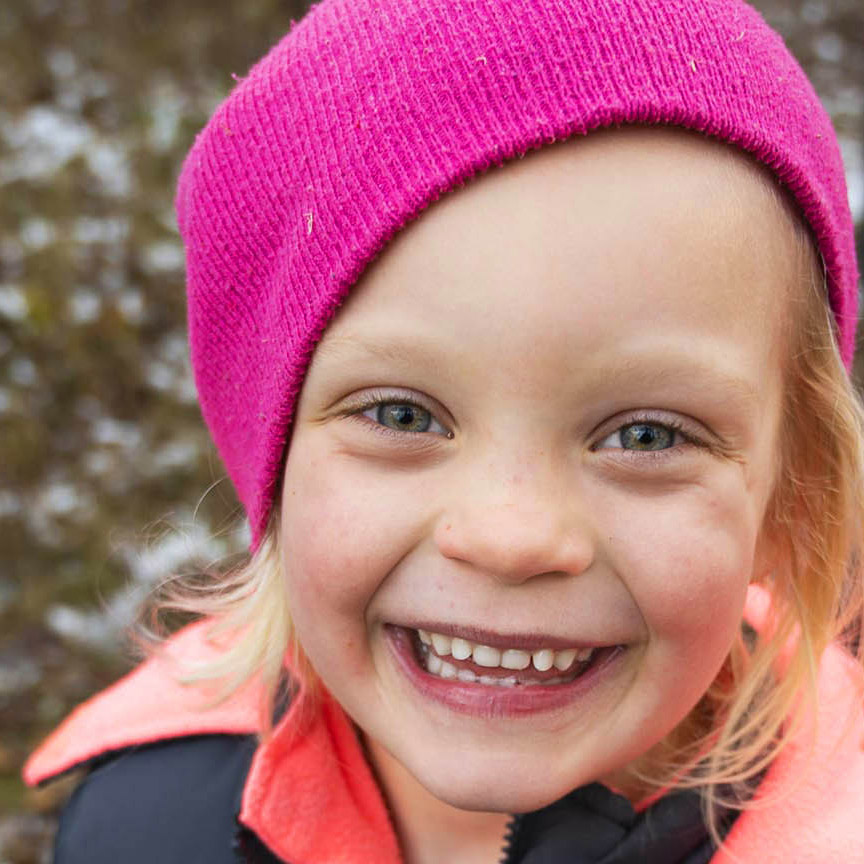 A young girl smiles while wearing a pink hat