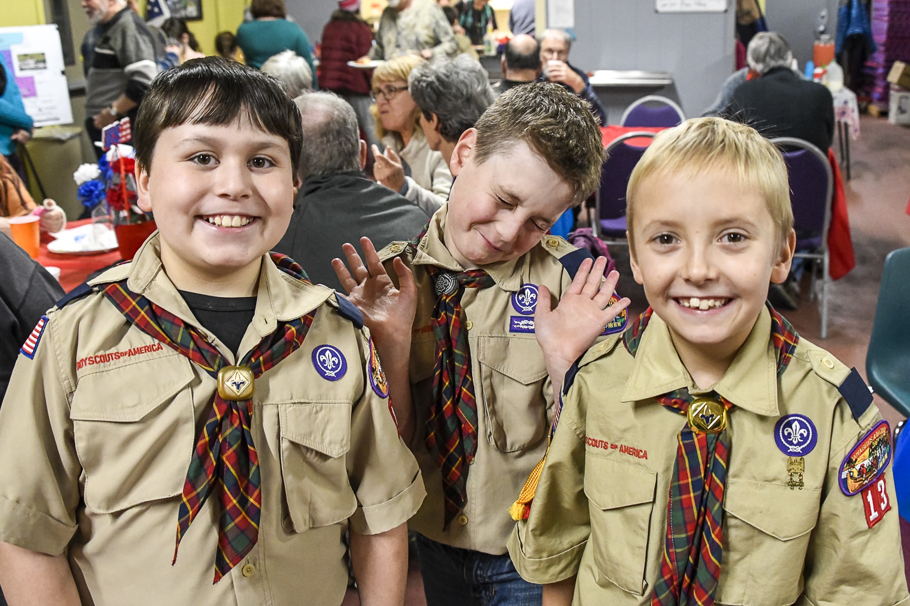 Three boys in boy scout uniforms smile in the Community Building at the GND REC, one holds his hands up to his face