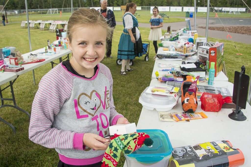 A young girl smiles while looking through items at a rummage sale outside of the GND REC