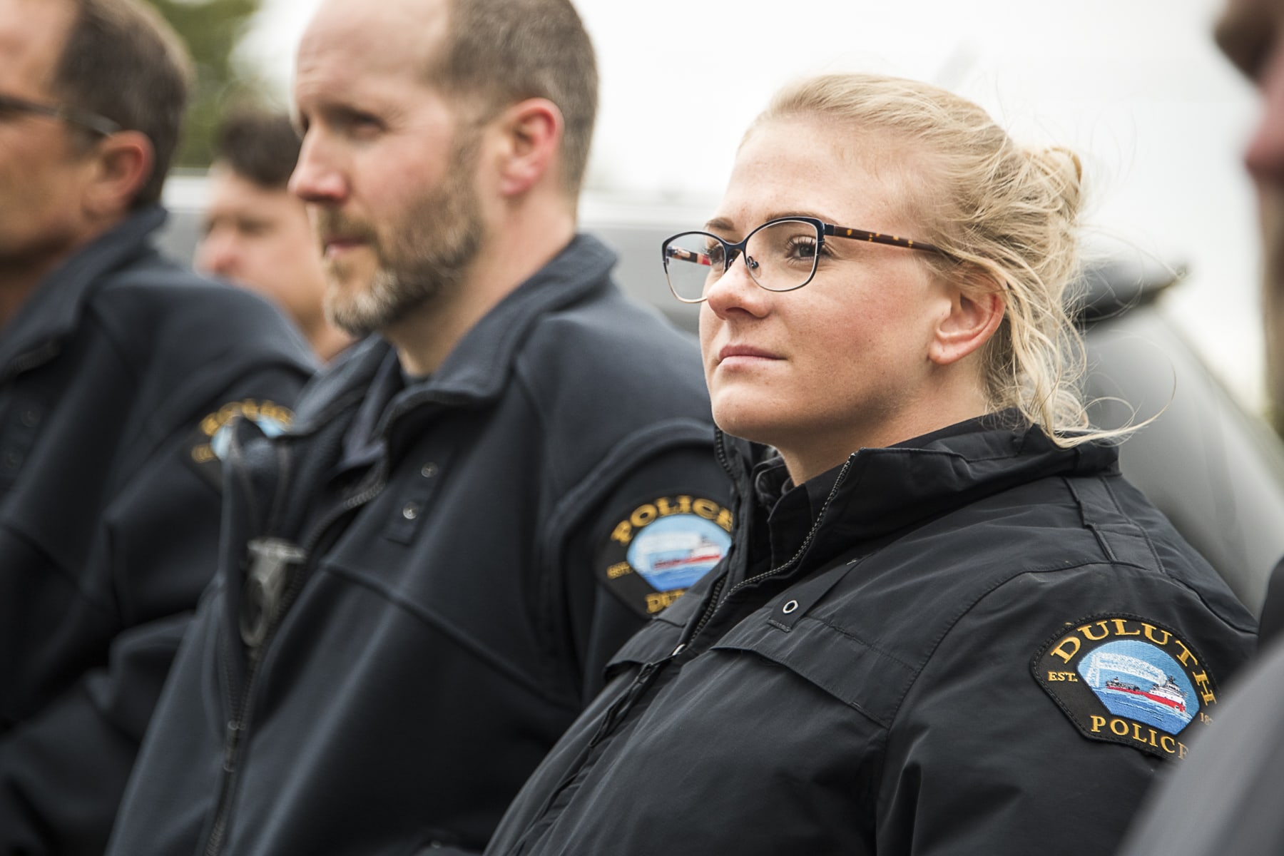 A man and a woman in police jackets look into the distance on a cloudy day
