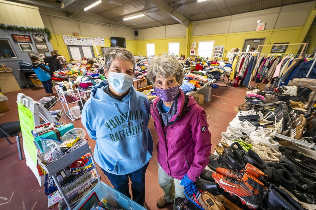 two women wearing masks smile in front of a rummage sale at the Community Building in the GND REC